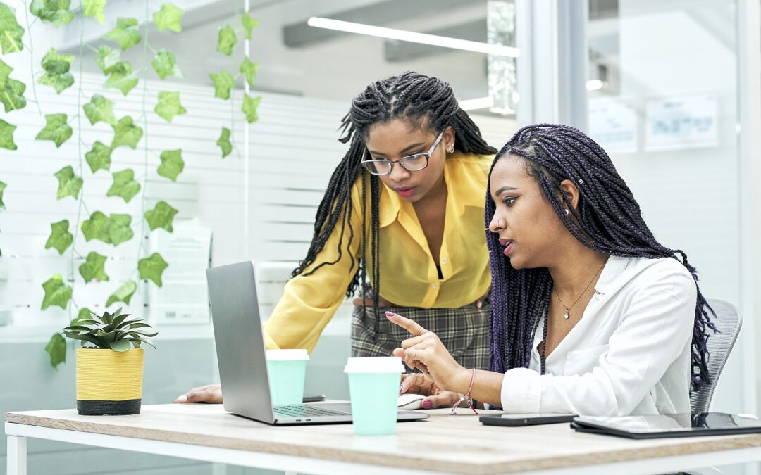 Two young black women reviewing analytical data on various electronic devices. I work in an office for millennial workers.