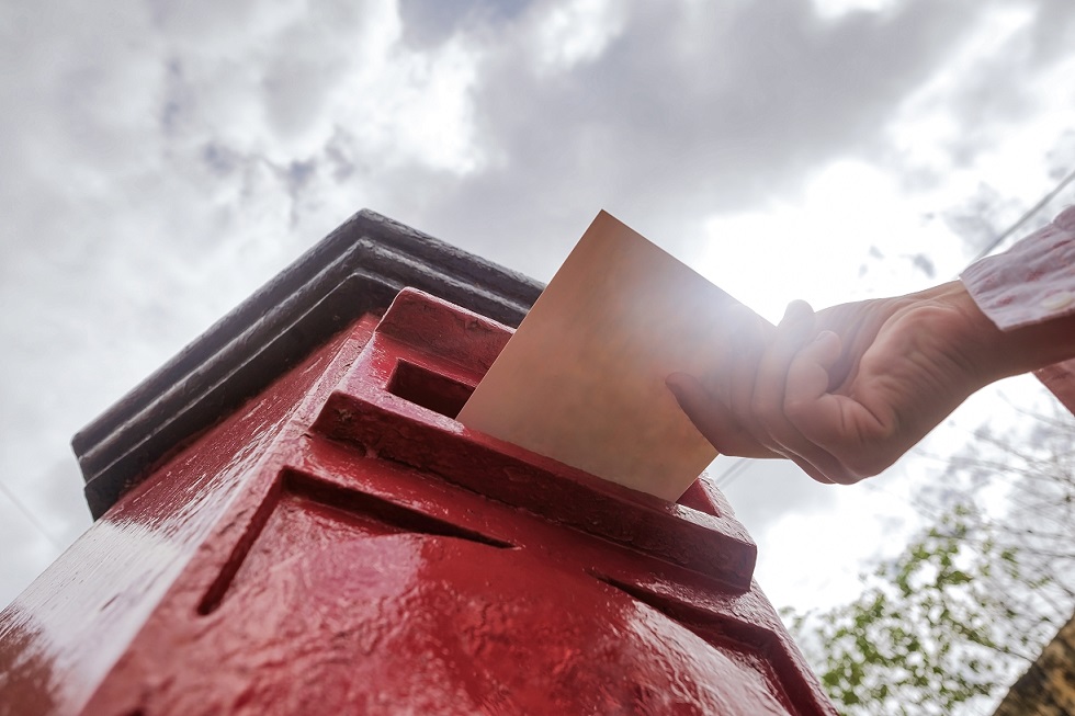 Closeup on a male hand putting a letter in a red letterbox. Concept of vintage type of communication. To send postcard from vacation or travel