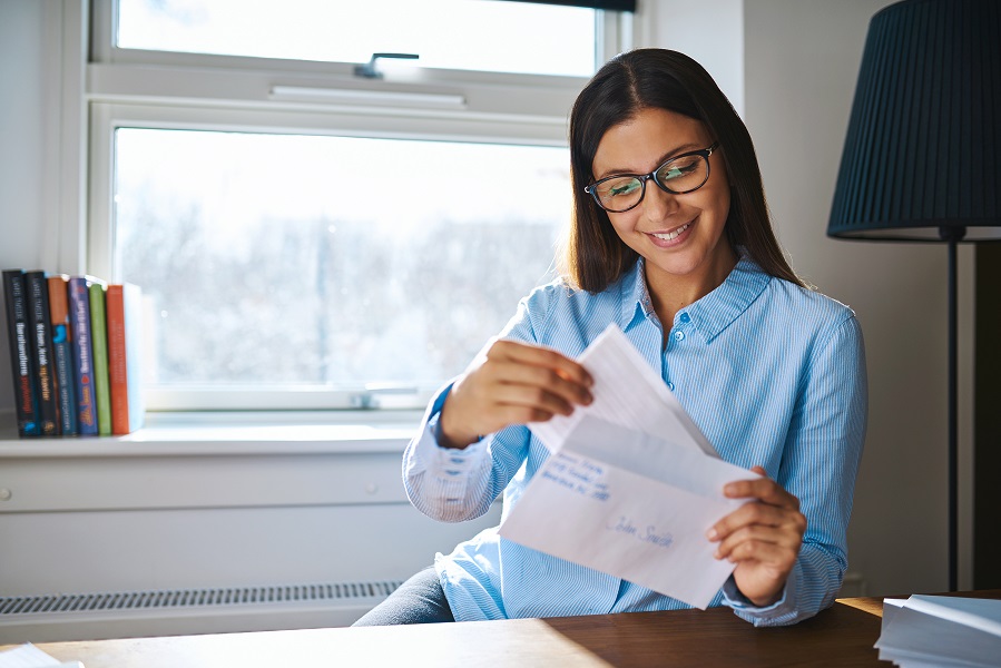 Young business entrepreneur checking her mail sitting at her desk at home with an open letter in her hand