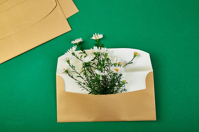 Gold envelope with a spring flower arrangement on green background. Flat lay, top view. Opened envelope. Festive greeting concept